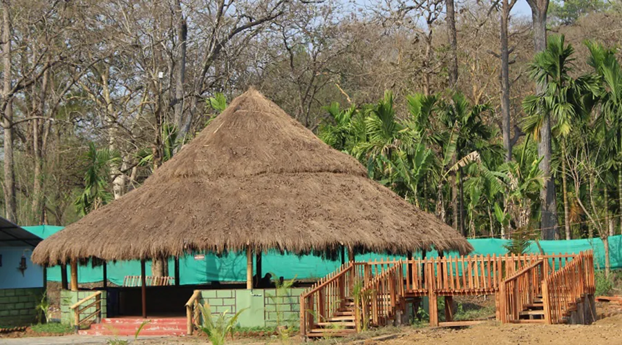Thatched dining pavilion and wooden walkway at Jungle Nest Dandeli