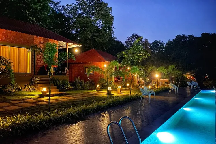 Cottages and lit pool at Tusker Trails Resort Dandeli