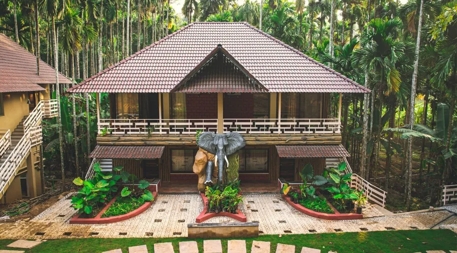 Cottage exterior with elephant sculpture and areca palms at Woodpecker Homestay Dandeli