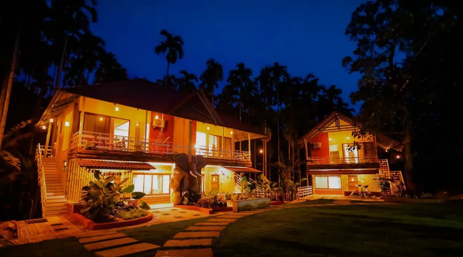 Night view of lit cottages among palms at Woodpecker Homestay Dandeli